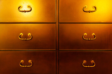 Chest of drawers in copper-gold color with antique handles, close-up.