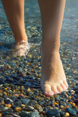 Female feet in sea water on a pebble in summer. Travel concept. Top view, copy space, relaxation in nature, swimming in the sea. Vertical orientation, selective focus