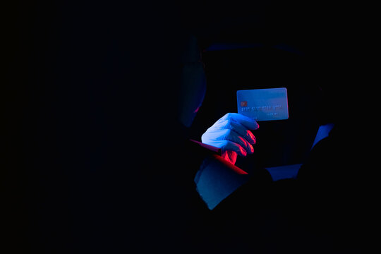 Fee-for-service medicare. Health insurance payment. Red blue neon light doctor hand holding credit card in black breakthrough hole ripped wall isolated on dark copy space background.