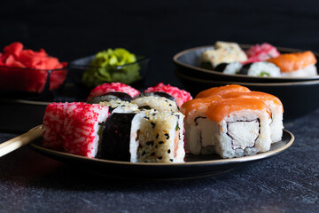 Sushi rolls lie on black plates on dark background, side view, horizontal