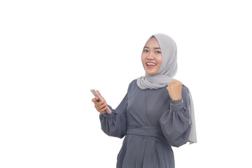Happy asian muslim woman standing while holding a mobile phone and clenching her hand.
