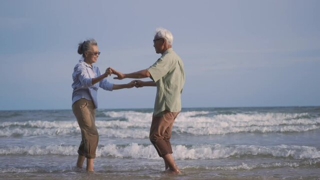 Happy Asian senior man and woman couple smile dancing resting relax on the beach honeymoon family sunny day, Romantic elderly enjoy travel summer vacation, plan life insurance at retirement couple