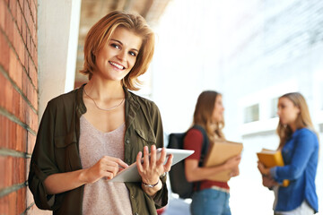 Technology is helping me excel at college. Portrait of a smiling female university student standing on campus using a digital tablet with friends in the background.