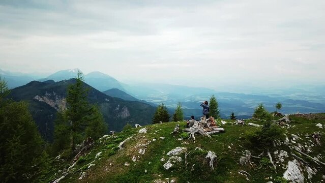 An active hiking couple having a rest with a panoramic lookout from from Hochpetzen in the Karawanks in Carinthia, Austria. Aerial view on the valley and the surrounding mountains. Aerial photography
