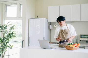 パソコンを見ながら料理する男性（笑顔）  © buritora