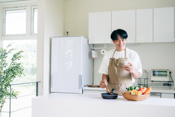 スマホを見ながら料理する男性（笑顔）  © buritora