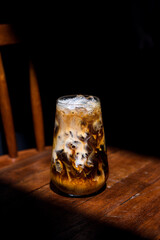Ice coffee on a wood table with cream being poured into it showing the texture and refreshing look of the drink