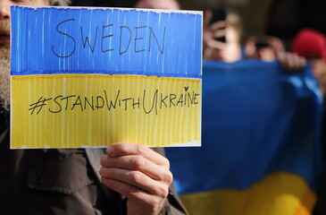 Protester with cardboard in national Ukrainian colours and slogan SWEEDEN STAND WITH UKRAINE while...