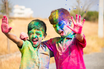 cheerful two Indian kids shouting by looking at camera after playing holi - concept of holi...