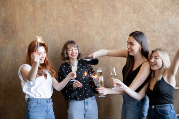 Group of young adult girlfriends drinking sparkling wine and firing sparklers, celebrating together...