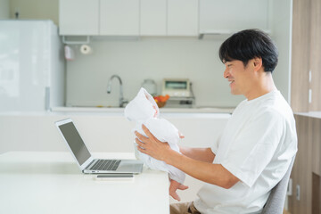 Obraz na płótnie Canvas 赤ちゃんを抱きながら仕事する男性 