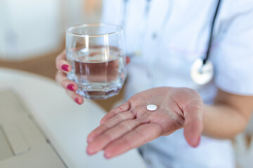 Female doctor having online therapy with her patient's, giving them advice while holding a pill and glass of water in her hands