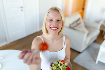 Portrait of attractive caucasian smiling woman eating salad. Young and happy woman eating healthy salad with green fresh ingredients indoors