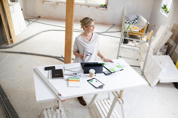 pretty young architect working on construction site in loft and standing by high table wearing...