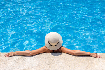 Femme au chapeau qui se détend dans l'eau au bord d'une piscine