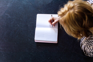 Naklejka premium On a black background there is a notebook in which a person with a pen in his hands makes a note
