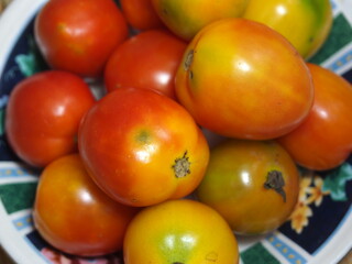 Close-up of fresh half ripe tomatoes on a melamine plate on wooden floor background