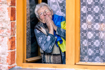 Ukrainian grandmother with flag on the face with fear suffering and praying peace during war conflict between Russia and Ukraine, invasion of Russia in Ukraine, glory to Ukraine