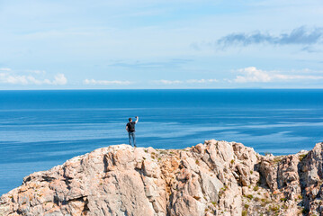 Fototapeta na wymiar Man with backpack standing on a rock at the end of earth using his smartphone for selfie photoshoot. Hiking or travel concept. Exploring the great outdoors. Beauty of nature 
