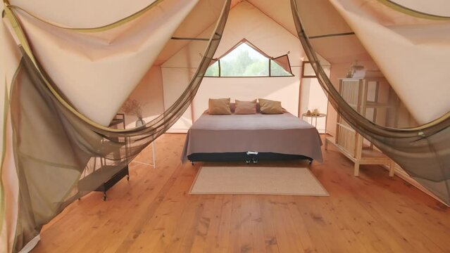 Dollying of classy terrace and bedroom with bed and chairs in glamping on summer day