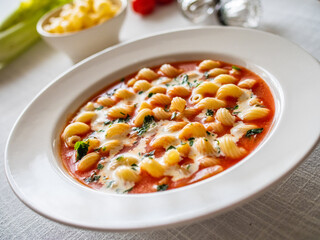 Tomato soup with cream, noodles and fresh parsley on white table
