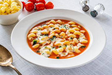 Tomato soup with cream, noodles and fresh parsley on white table
