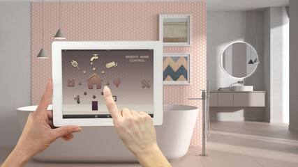 Smart remote home control system on a digital tablet. Device with app icons. Modern bathroom with bathtub and mosaic tiles in the background, architecture interior design