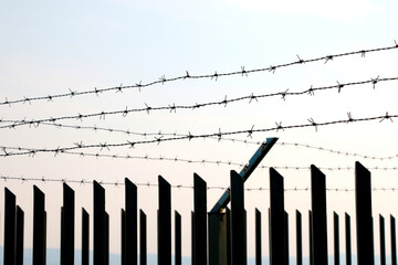 Fence on the border with barbed wire at sunset.