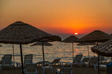 Fototapeta na wymiar tourists sunbatting under straw umbrellas. REflection of amazing sunset