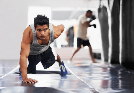 Pure fierce strength. Portrait of a focused young boxer doing push-ups in the gym.