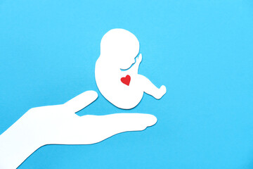 Paper silhouette of a human embryo on a doctor's hand. Flat lay, place for text.