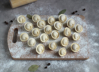 homemade dumplings on a cutting board in rows of flour, pepper and bay leaf