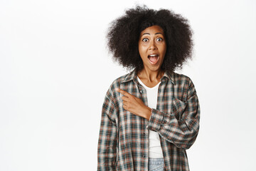 Enthusiastic Black woman pointing left, showing promo information aside, copy space for logo, banner or text, standing over white background