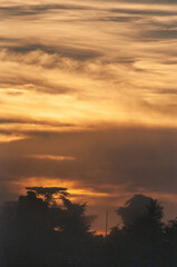 Dreamlike image of the setting sun breaking through a cloud layer and showing tree silhouttes.