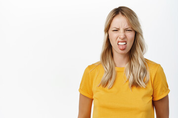 Dislike and aversion. Young woman grimaces and look with disgust at smth bad, stands over white background