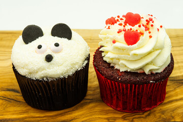 Two chocolate cupcakes with panda face cream shape and heart decoration on wood on white background with copyspace