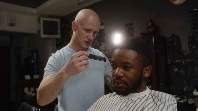 Caucasian hairdresser combing brown curly hair to young african american man