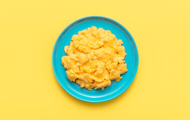 Scrambled eggs in a blue plate, top view on a yellow table.