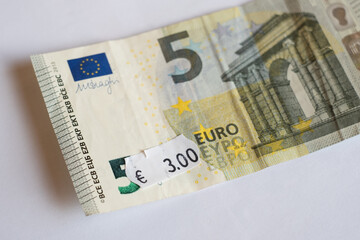 Five euro banknote with three euro price tag. Selective focus on label. Inflation in Europe, hyper inflation, devaluation concept.