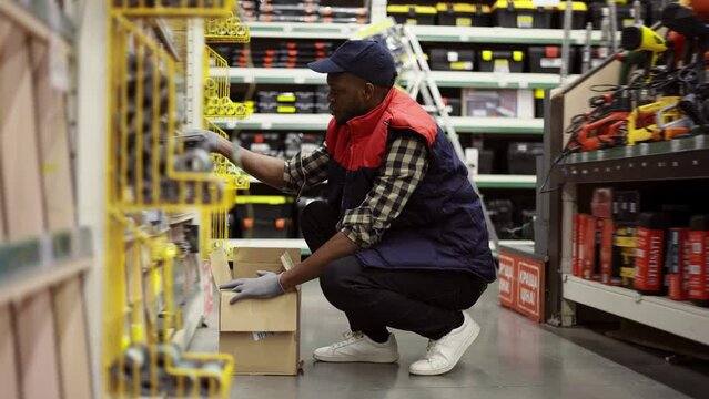 Male worker refill goods on lower shelves of hardware store