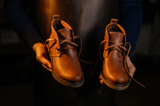 Photo of a pair of quality men's leather shoes in the hands of the master who made them. Manufacturing industry and footwear production concept