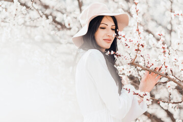 Portrait of pretty brunette girl posing against the spring blooming trees in hat.