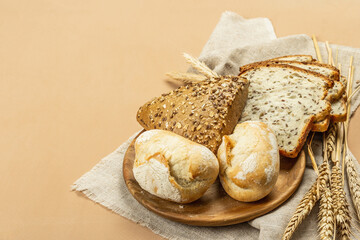 Freshly baked bread with wheat ears, buns, and toasts. Assorted bakery on light beige background