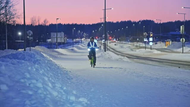 The man on a bicycle in a winter evening. Light is reflected from clothing reflectors and bicycle wheels. Safe cycling in the dark time.