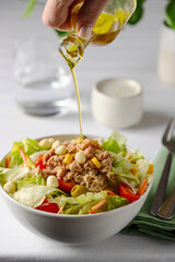 Hand pouring oiloive oil into the  bowl with Fresh tuna salad. Close up