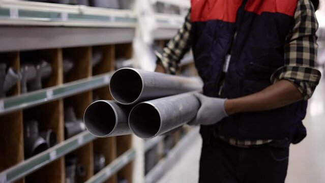 Unrecognizable worker walks with water pipes in plumbing or hardware store, cropped