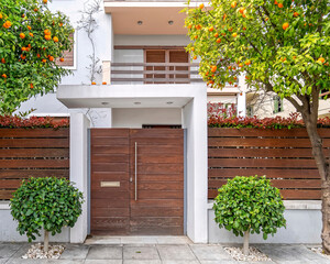 modern house with wooden fence and front door between citrus trees