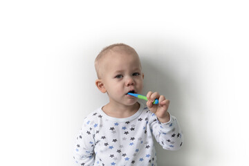 A little boy stands against a white wall, dressed in a T-shirt with stars, brushes his teeth and takes care of his mouth.