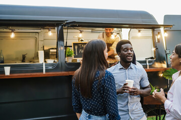 Multiracial people having fun drinking in front of food truck outdoor - Focus on african man face