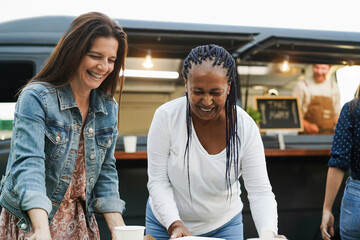 Multiracial women eating at food truck restaurant outdoor - Focus on african female face